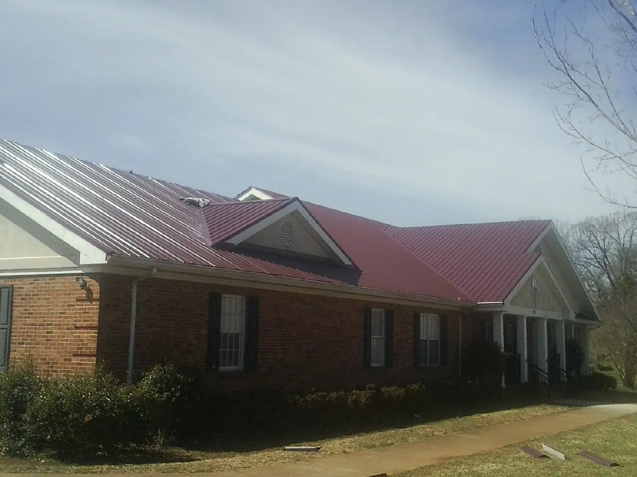 Red metal roof with gabled entries on a long brick building, from a Hail Damage Roof Repair job in Ferndale