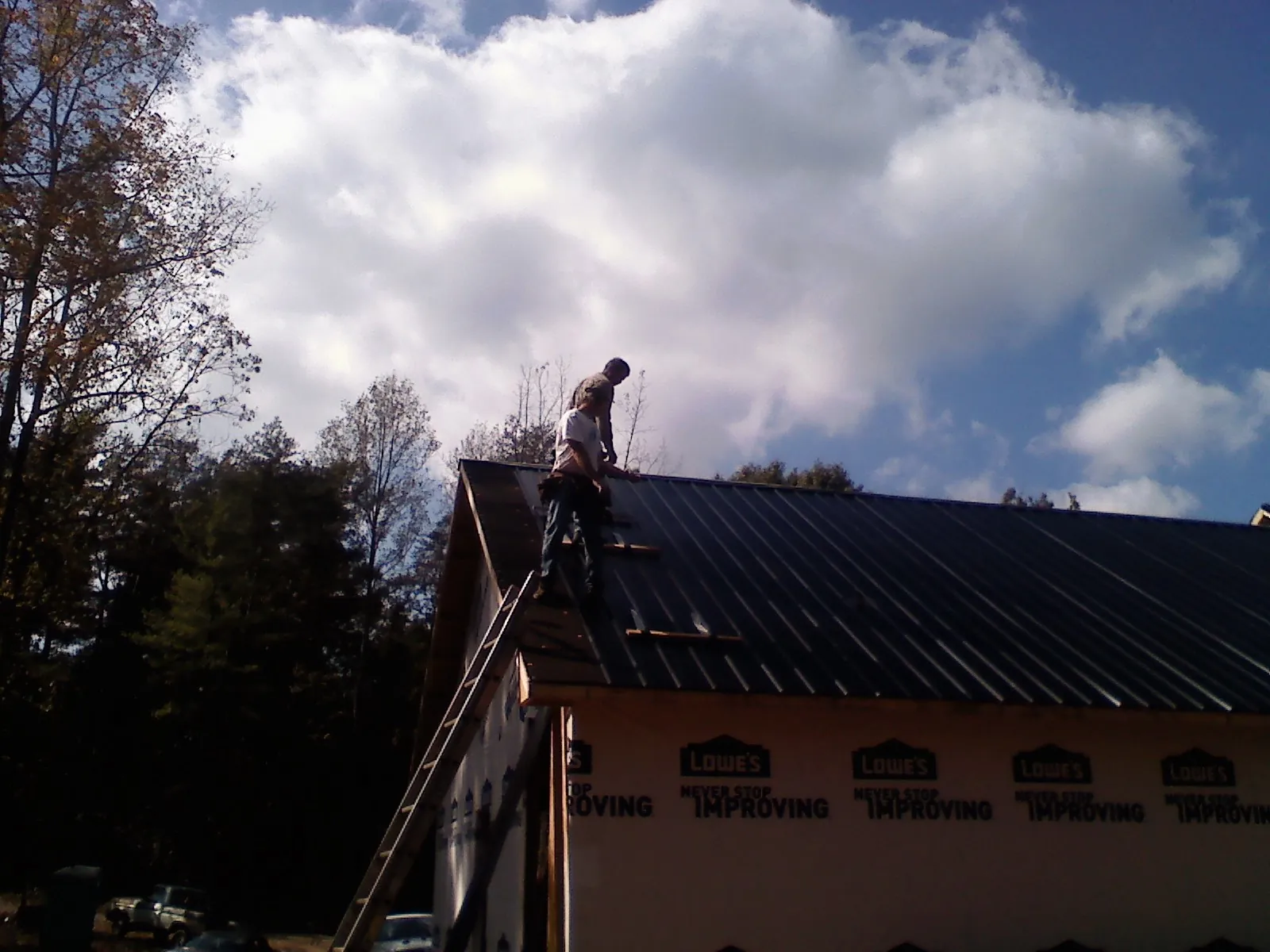 Roofer fastening dark metal panels high against a cloudy sky, from a Roof Inspection job in Ferndale